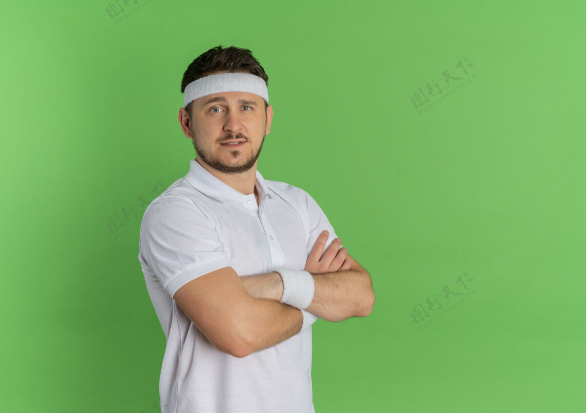 人身穿白衬衫 头箍 双手交叉放在胸前 自信地站在绿色墙壁上的年轻健身男子人表情头带