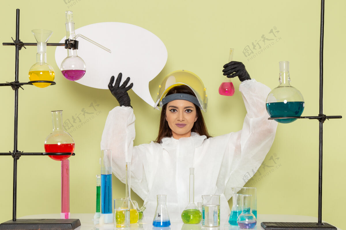 外套正面图身着特殊防护服的女化学家手持白色标志和绿色表面上的溶液医学科学化学家