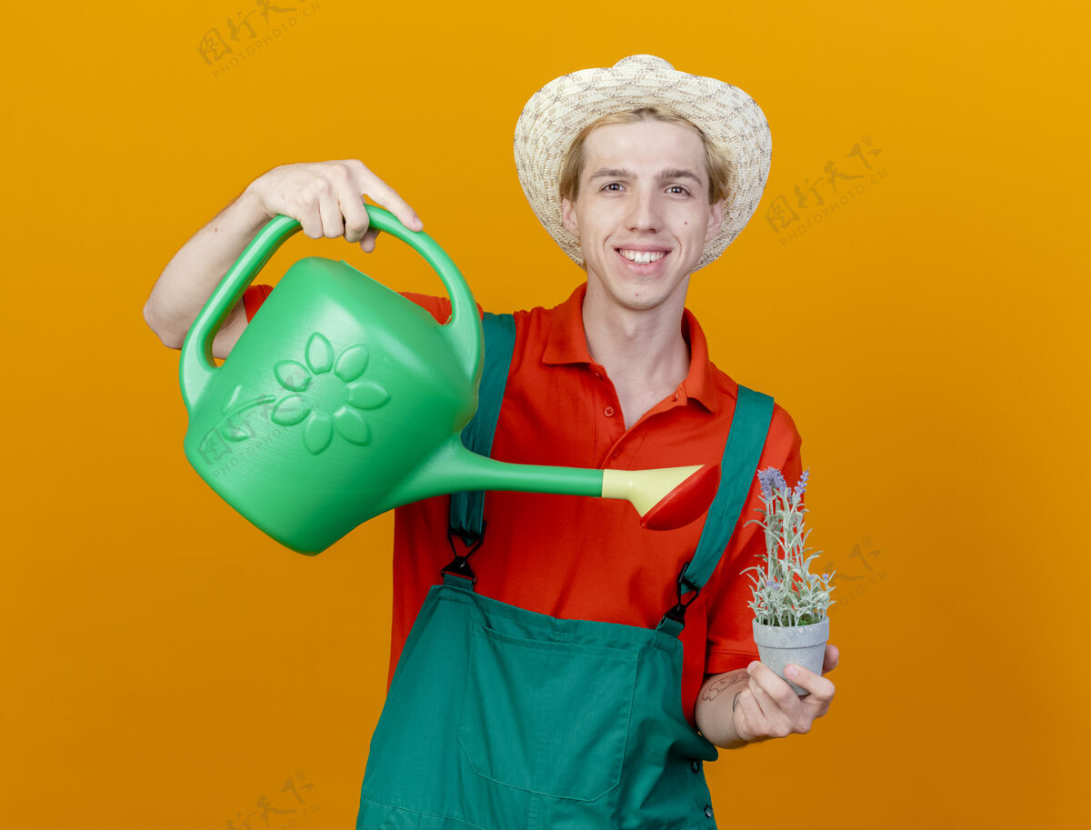 穿快乐的年轻园丁 穿着连体衣 戴着帽子 手里拿着浇水罐浇水连身衣脸