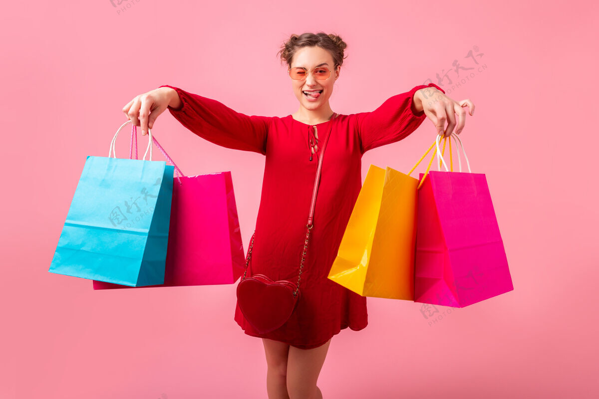 女孩迷人快乐搞笑情感时尚女性购物狂身着红色新潮连衣裙手捧五颜六色购物袋在粉色墙壁上孤零零出售 销售兴奋 春夏时尚潮流模特人商店
