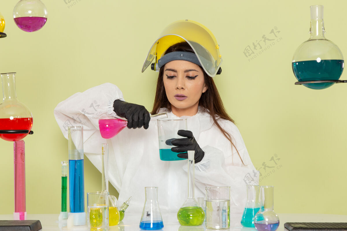 女性前视图穿着特殊防护服的女化学家在浅绿色表面上用不同的溶液工作外套科学正面