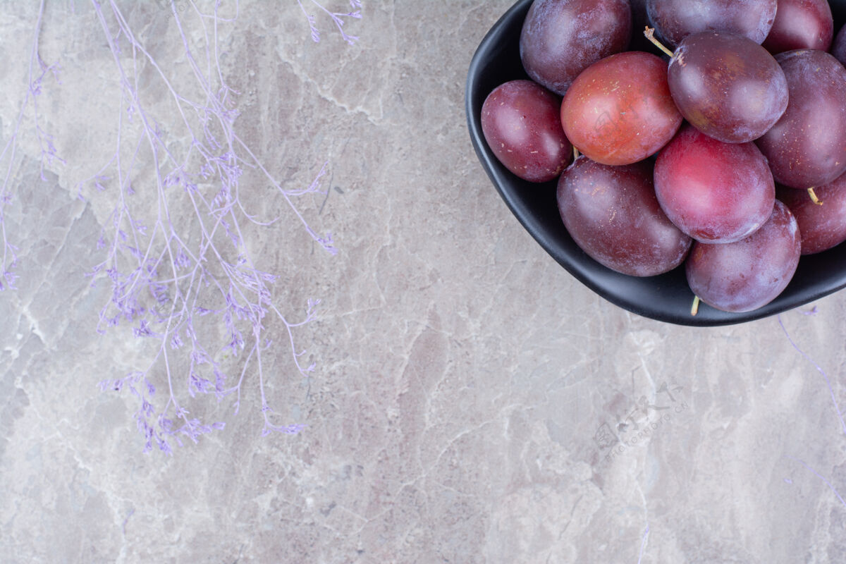 新鲜石头背景上的黑李子碗水果李子紫色