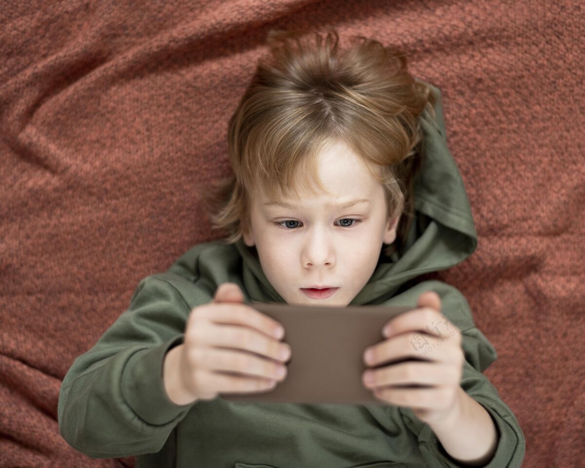 设备小男孩在床上使用智能手机的俯视图业余爱好娱乐儿童