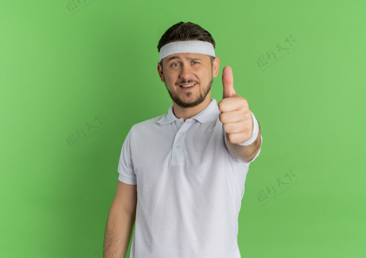 年轻身穿白衬衫 头箍微笑的年轻健身男子站在绿色的墙上 朝前竖起大拇指男人运动装人