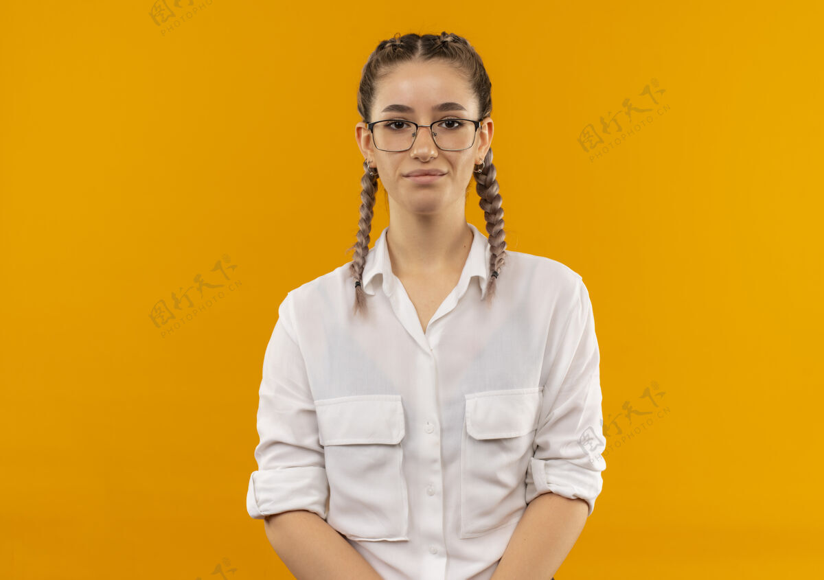 自信戴着眼镜 梳着辫子 穿着白衬衫的年轻女学生站在橙色的墙上 带着严肃自信的表情望着前方表情学生辫子