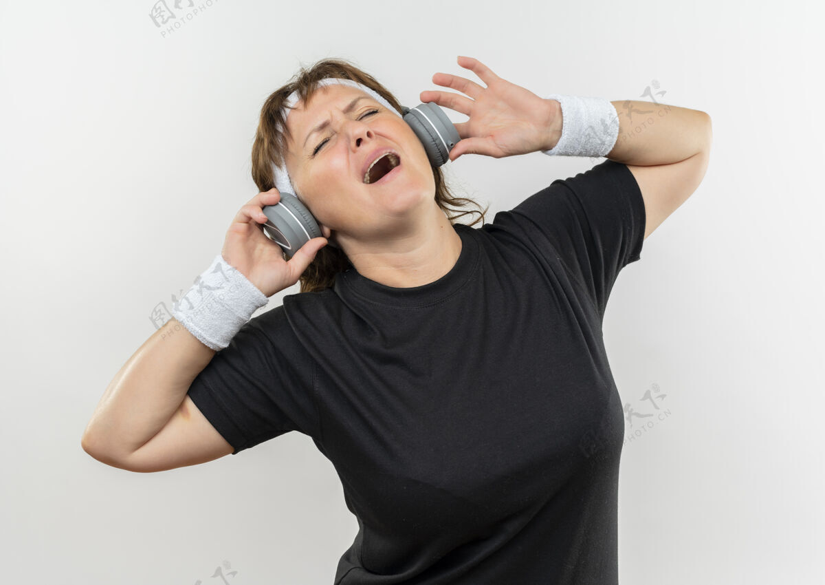 头带中年运动女性 身穿黑色t恤 戴着头带和耳机 站在白墙上疯狂地享受着音乐享受年龄运动