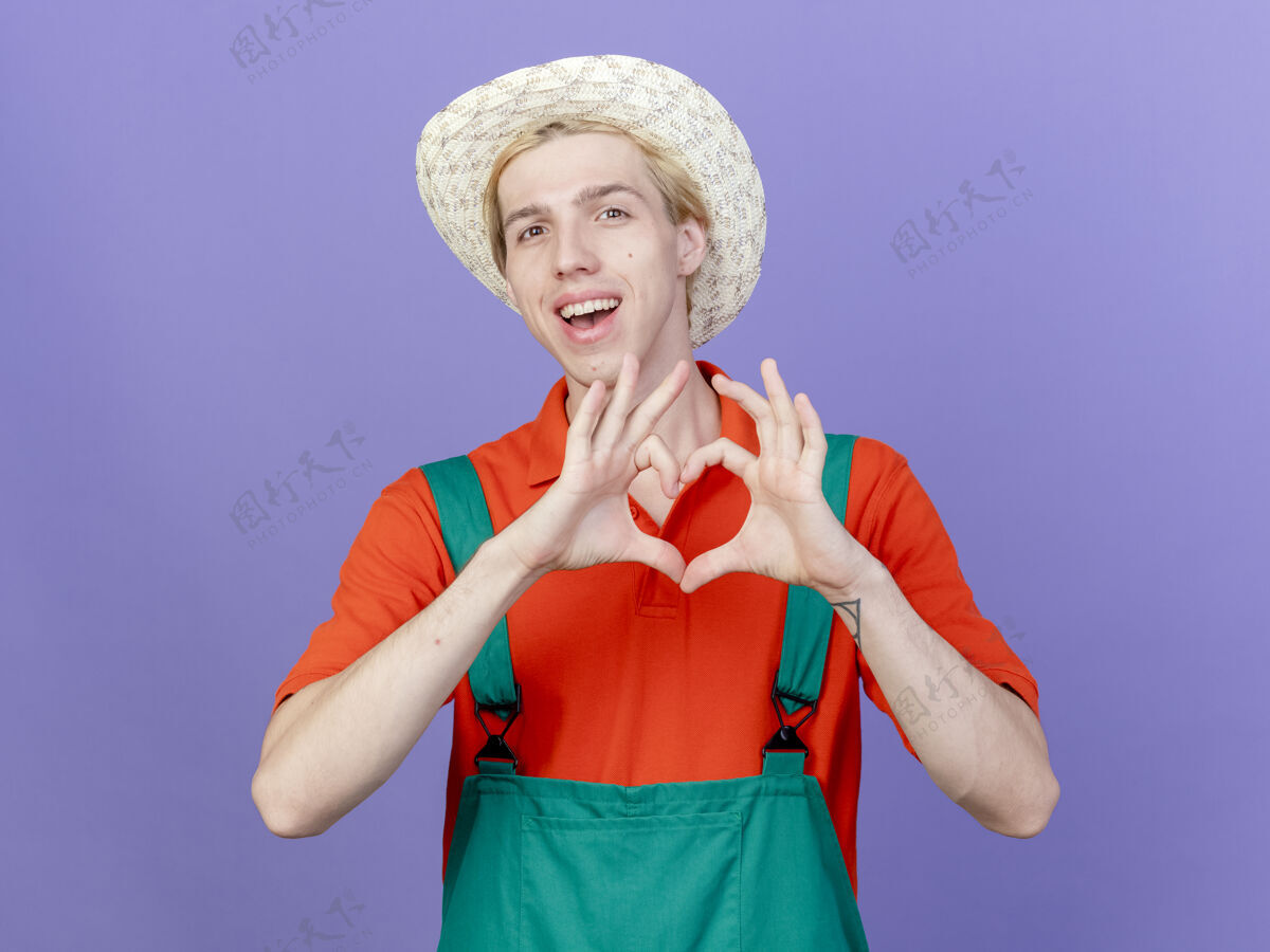 年轻年轻的园丁 穿着连体衣 戴着帽子 用手指做着手势穿心手势