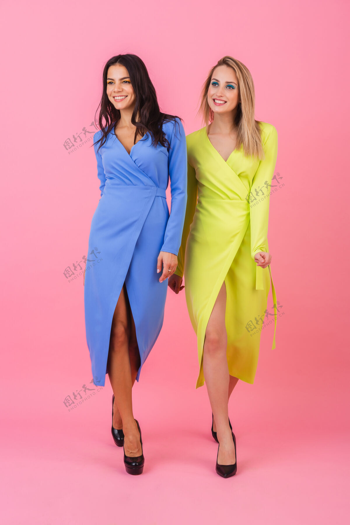 运动两个时尚性感的微笑迷人的金发和黑发女子在粉红色的墙上摆姿势在蓝色和黄色的时尚多彩的礼服 夏季时尚潮流外套夹克模特
