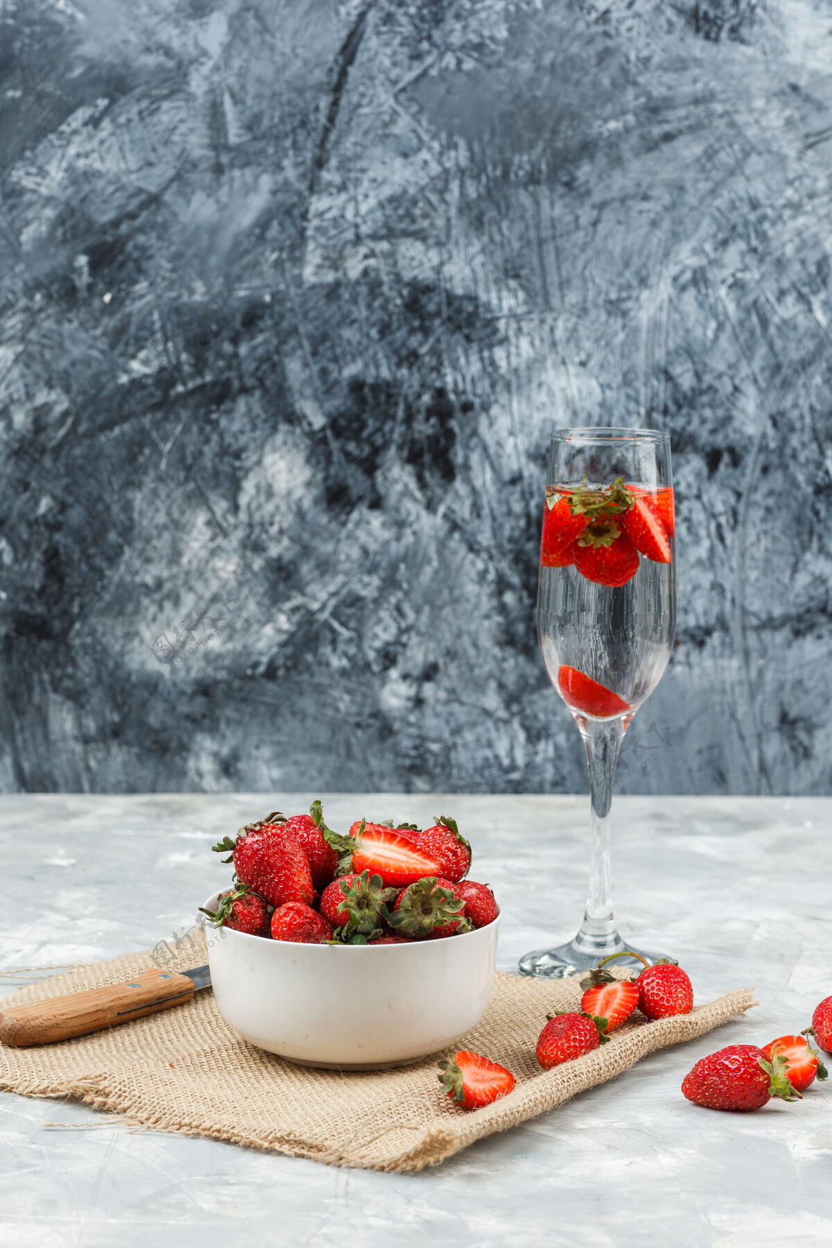 美味把一碗草莓放在一个袋子上 一杯饮料放在白色和深蓝色的大理石表面垂直食物水果营养