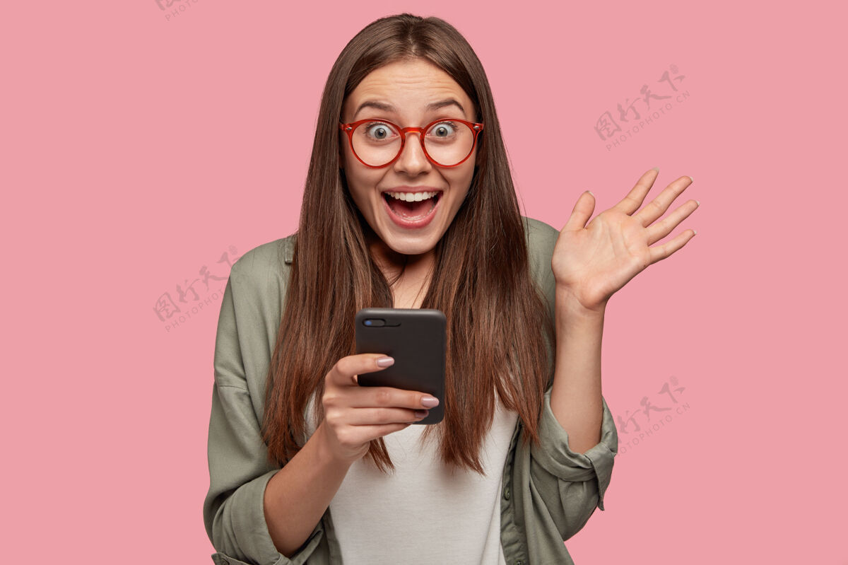 信息惊讶的高加索女孩手持现代手机 展示手掌眼镜设备手机