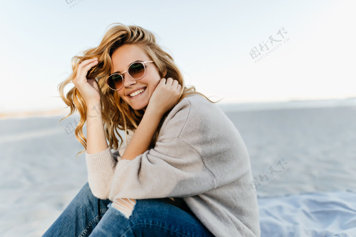 模型秋天的早晨 坐在沙滩上的黛比奈尔·布林德女士美丽的卷发女子在海上微笑的户外肖像海岸线寒冷肖像