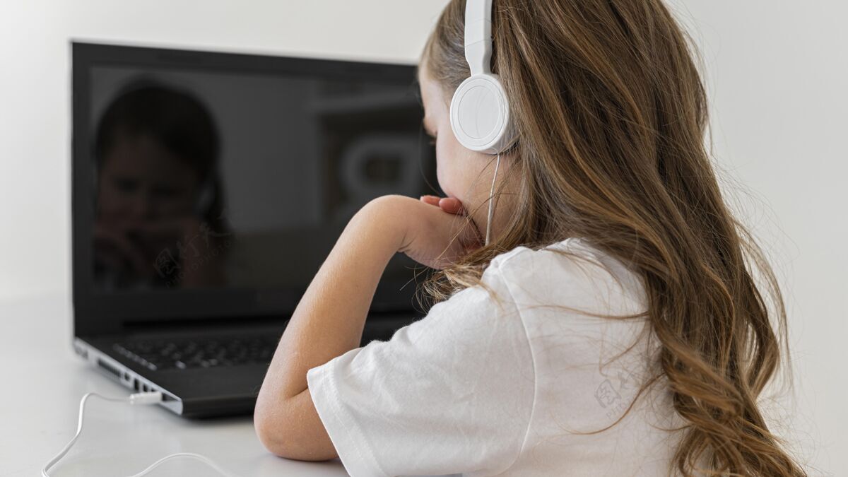 孩子小女孩使用带耳机的笔记本电脑的侧视图科技女孩笔记本电脑