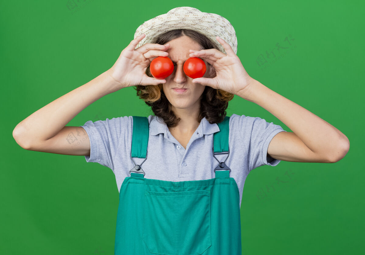 连身衣年轻的园丁 穿着连体衣 戴着帽子 手里拿着新鲜的西红柿遮住眼睛新鲜站着帽子