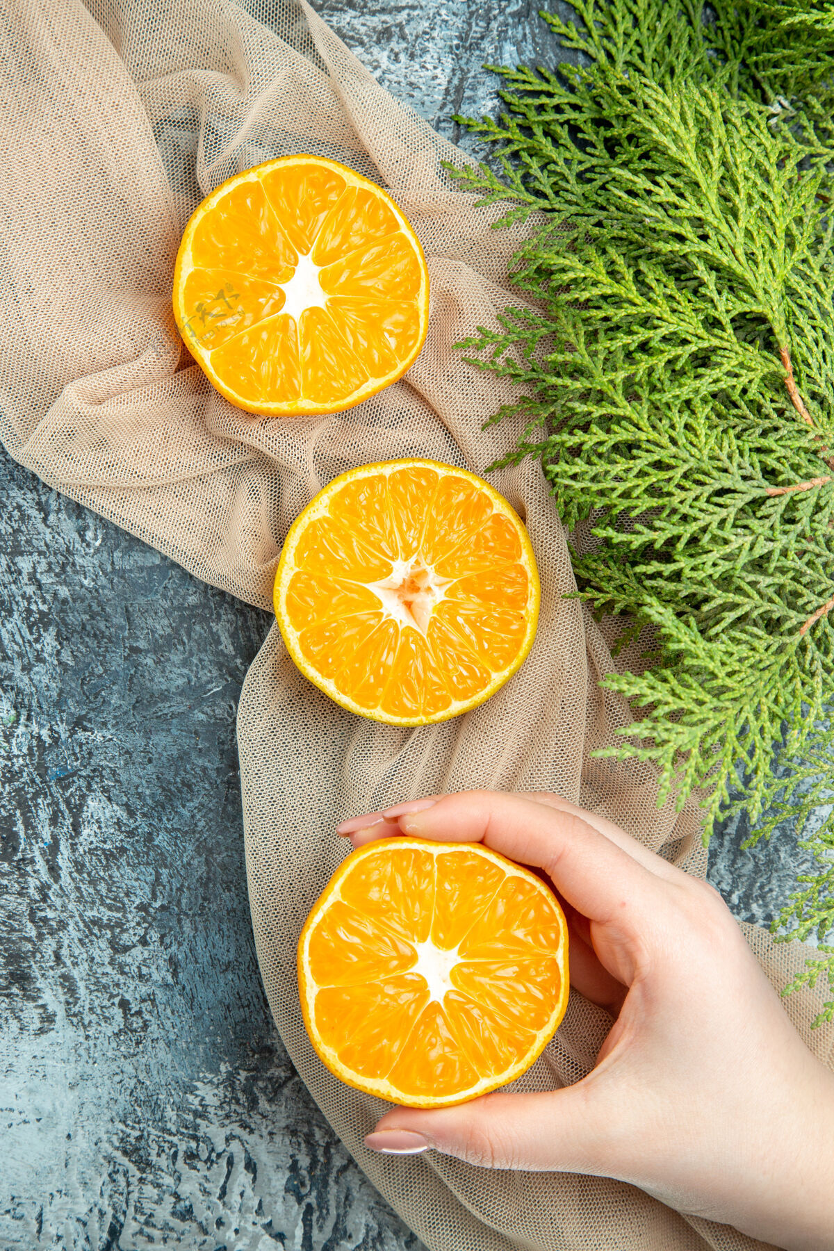 柠檬俯视图切割橙色在女性手松果在米色披肩在黑暗的表面新鲜果汁甜橙