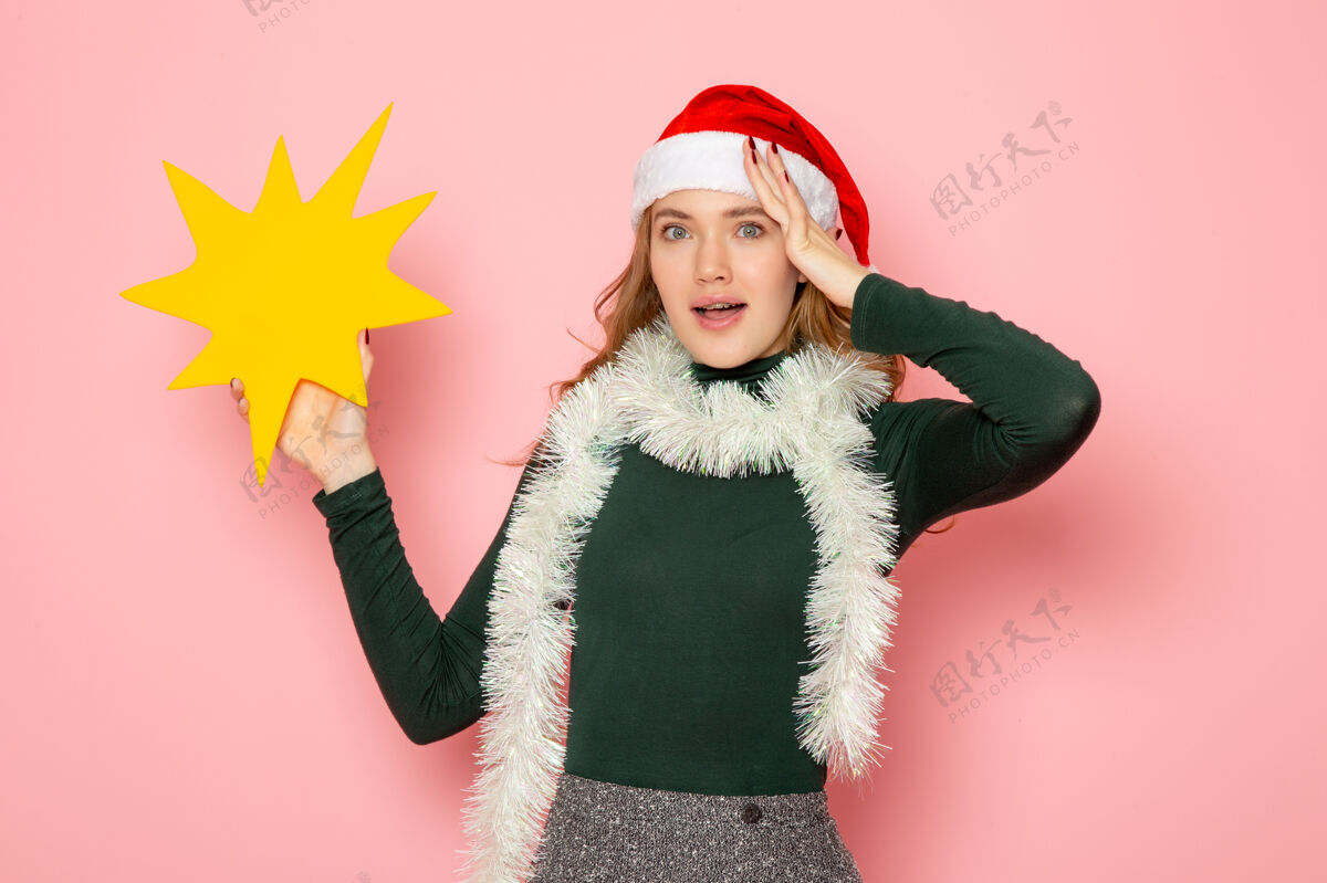 肖像正面图年轻女性手持粉色墙壁上的黄色大人物模型节日圣诞新年感慨年轻的女性圣诞节围巾