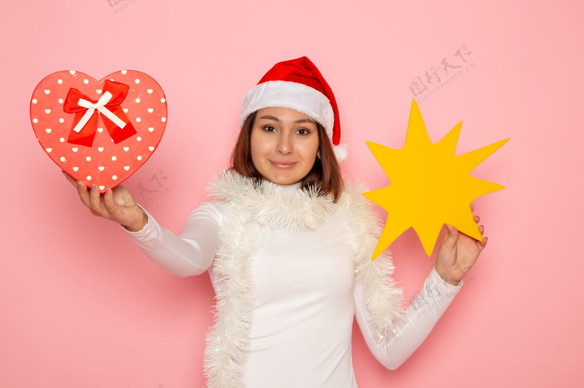 快乐正面图年轻女性手持黄色的身影 在粉色的墙上呈现圣诞色彩的节日新年时尚风景漂亮年轻的女性