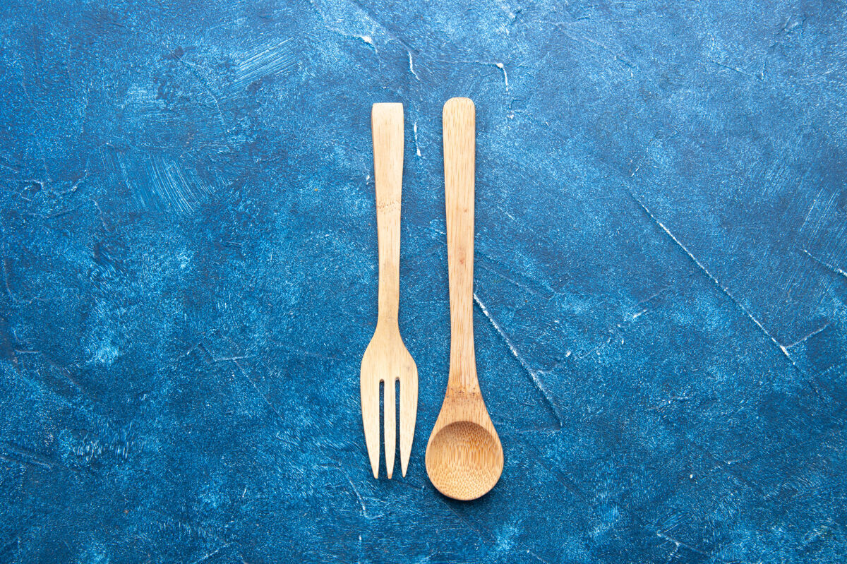 叉子蓝色桌子上的木制叉子勺子顶视图 有自由空间套装烹饪金属