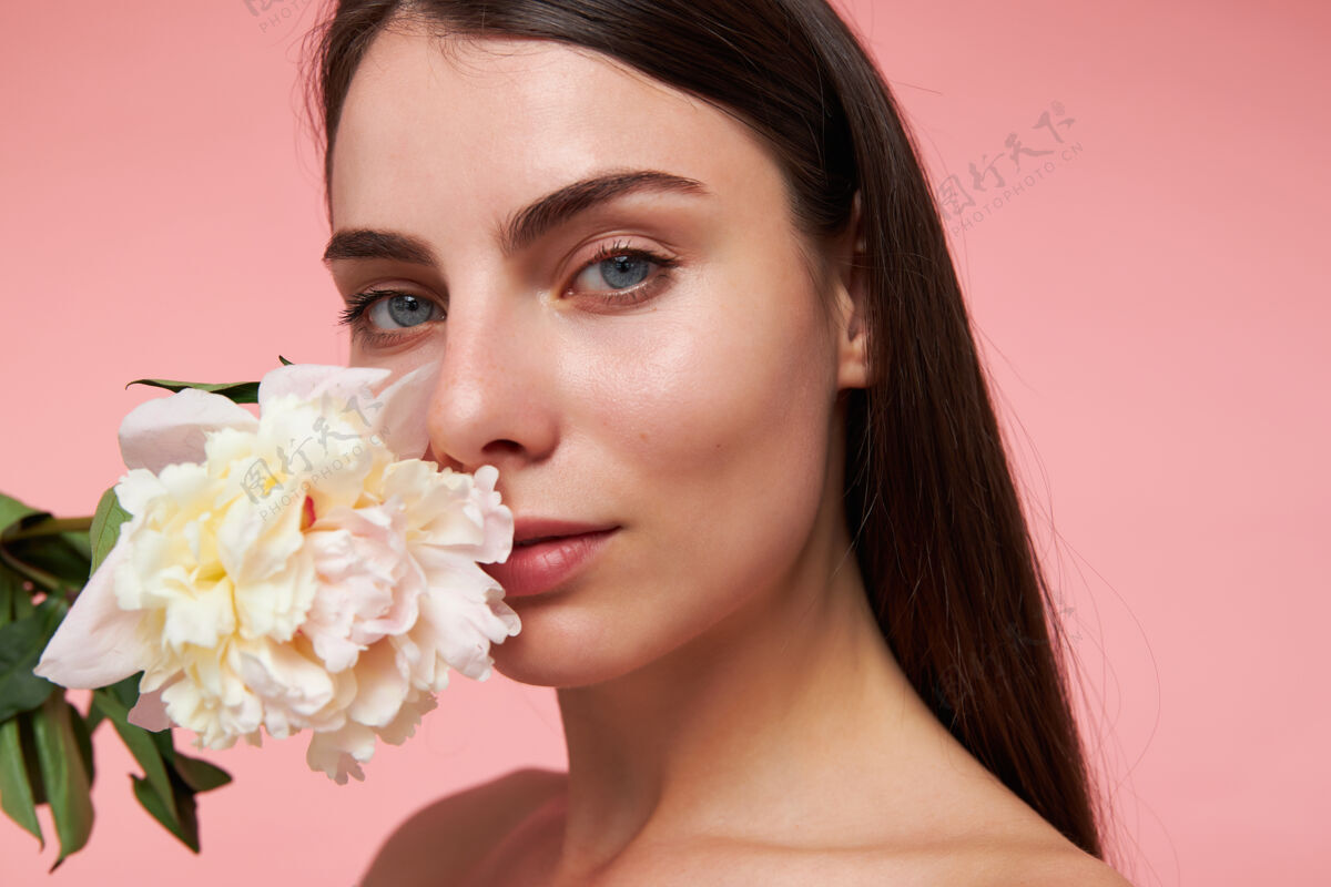 模特漂亮的女人 漂亮的女孩 深色长发 健康的皮肤 拿着一朵花放在脸旁看着 特写 隔离在粉彩粉色的墙上年轻姿势年轻