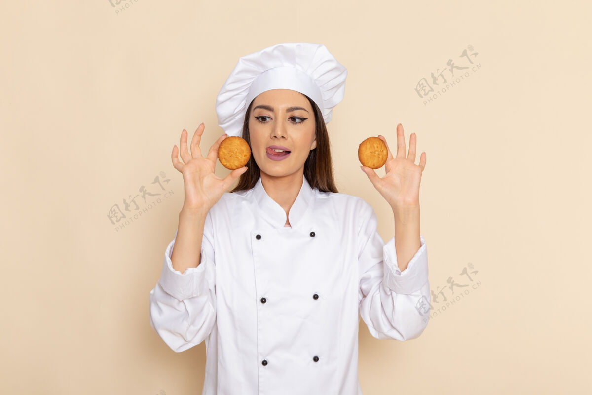 工作身穿白色厨师服的年轻女厨师正拿着饼干站在浅白的墙上女性人工作
