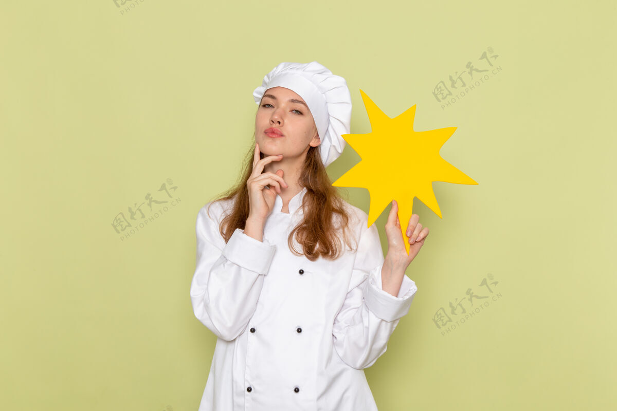 成人女厨师身穿白色厨师服 手持绿色墙壁上的黄色标志 正视图举行肖像前面