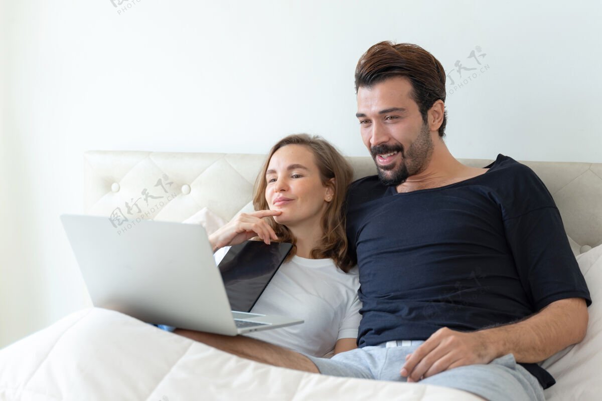 年轻英俊的丈夫和美丽的妻子在卧室里用笔记本电脑看电影 感觉很浪漫家庭爱情电影