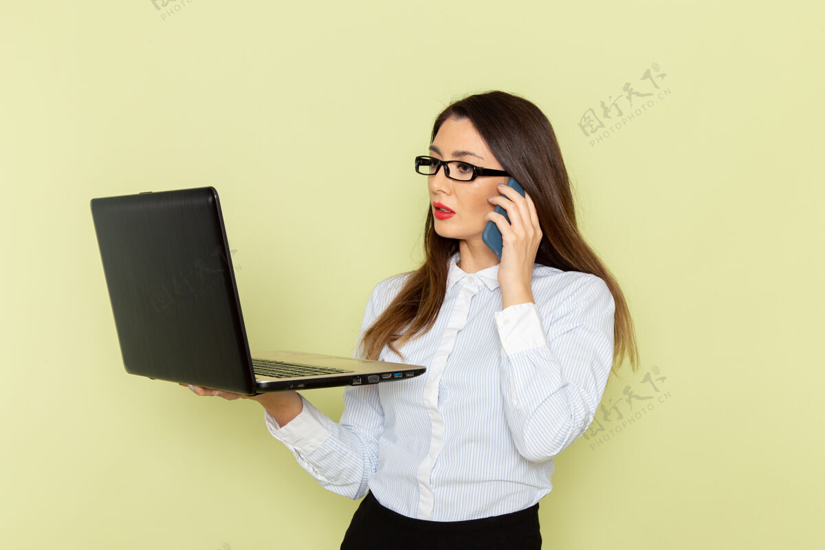 工作身穿白衬衫和黑裙子的女上班族的正面图绿色办公桌上拿着和使用笔记本电脑办公繁忙的工作妇女漂亮办公室电话