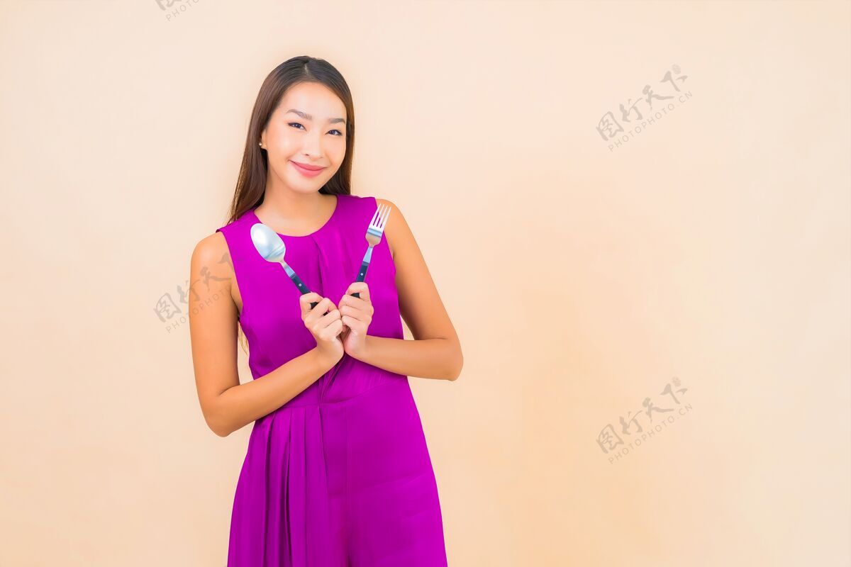 手肖像美丽的亚洲年轻女子与叉子和勺子准备在彩色背景上吃吃微笑T恤