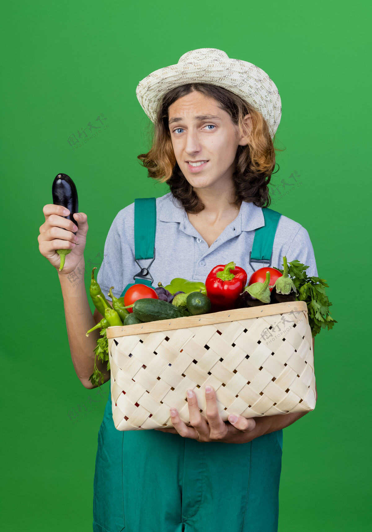 茄子年轻的园丁穿着连体衣戴着帽子拿着装满新鲜蔬菜的箱子困惑蔬菜新鲜
