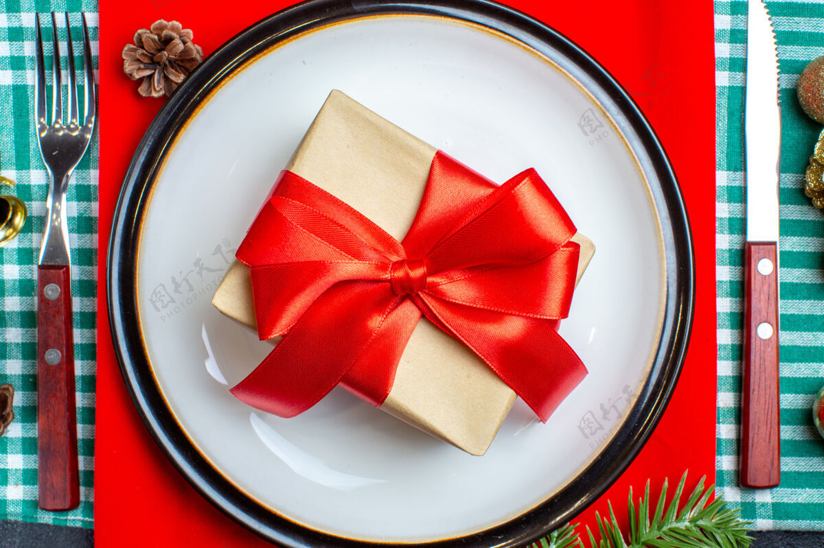 礼品盒顶视图美丽的礼品盒与蝴蝶结形状的红丝带在一个盘子和餐具上设置绿色条状毛巾圣诞节毛巾顶部