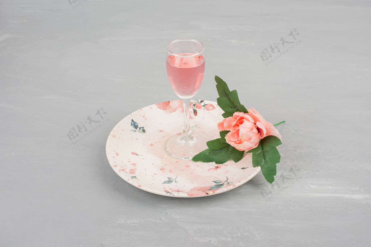 花一朵粉红色的玫瑰和一杯玫瑰红酒放在粉红色的盘子里玫瑰叶子花