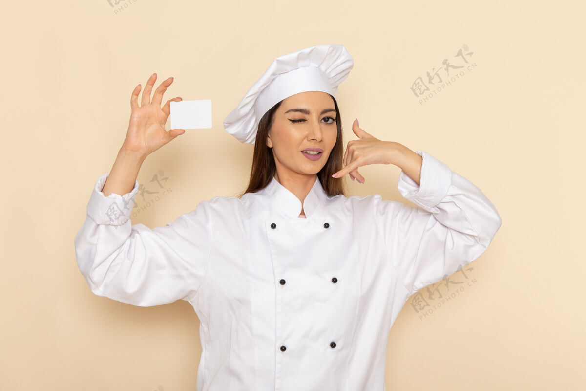 厨房身穿白色厨师服的年轻女厨师正拿着白色塑料卡站在白色墙上烹饪工作套装