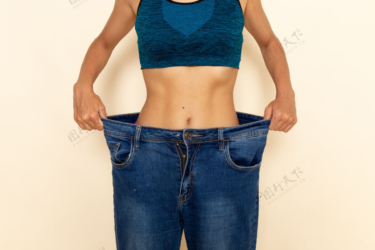 减肥年轻女性的前视图 穿着蓝色衬衫和牛仔裤 身体健康 墙壁为浅白色女运动私人教练