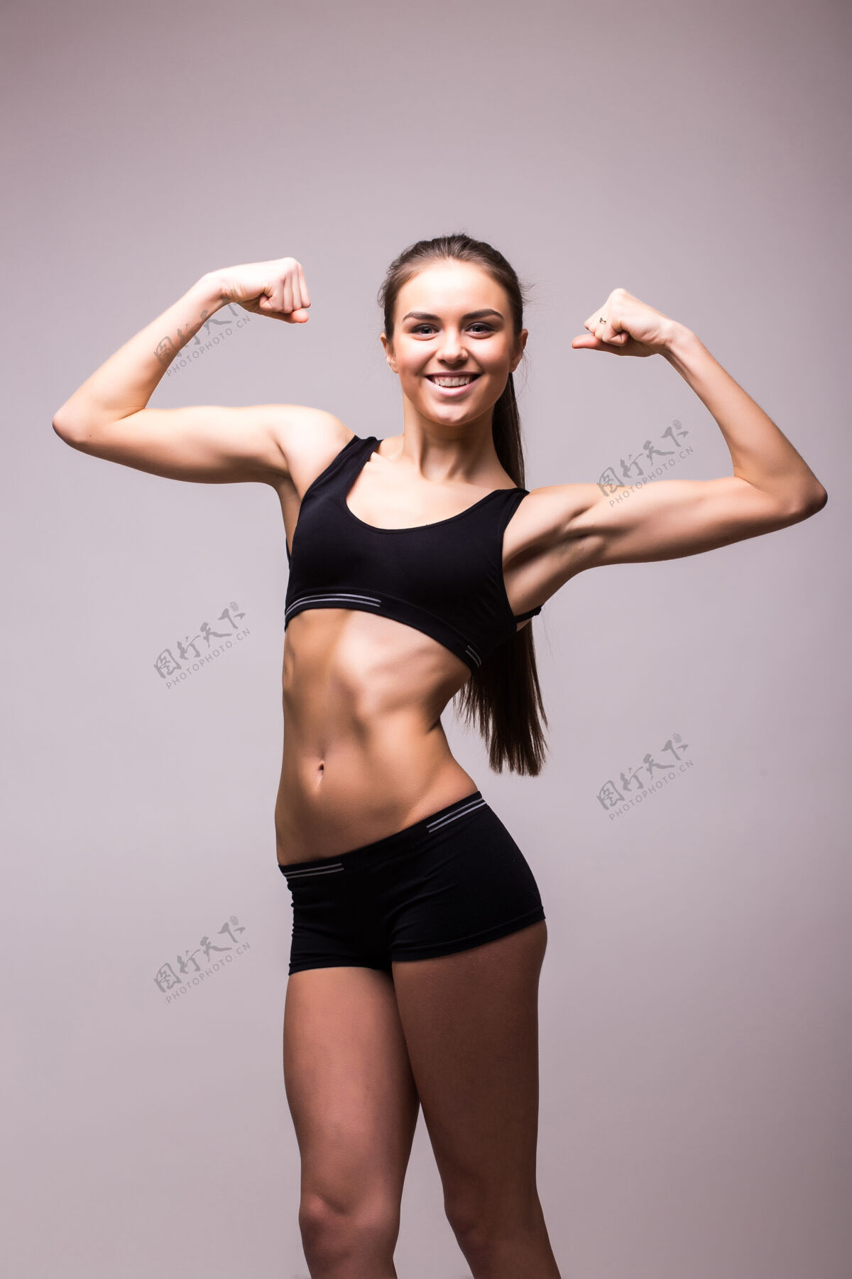 女坚强的年轻女子站在灰色的墙上锻炼健身房人