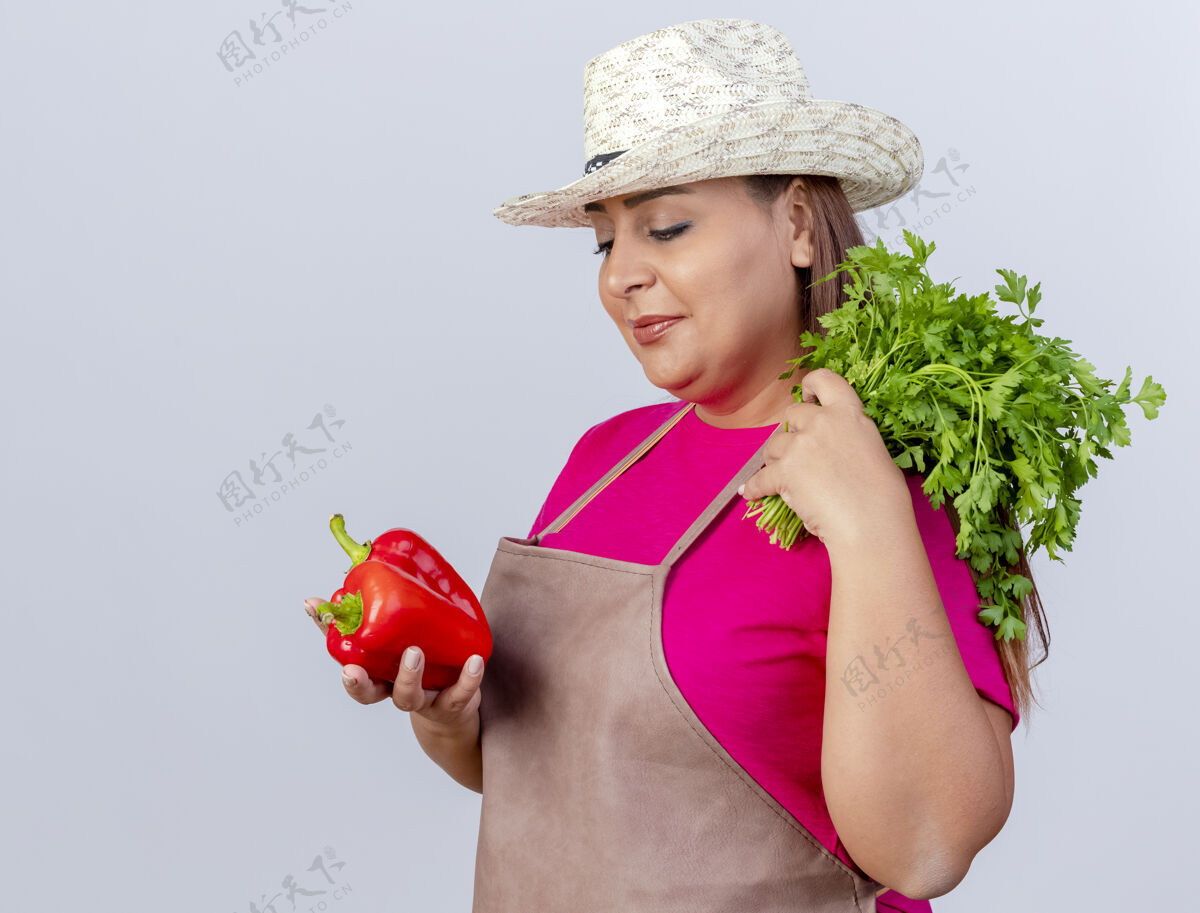 围裙围裙戴帽子的中年园丁 手里拿着新鲜的红甜椒和香草 站在白色的背景上 面带微笑地看着胡椒年龄看新鲜