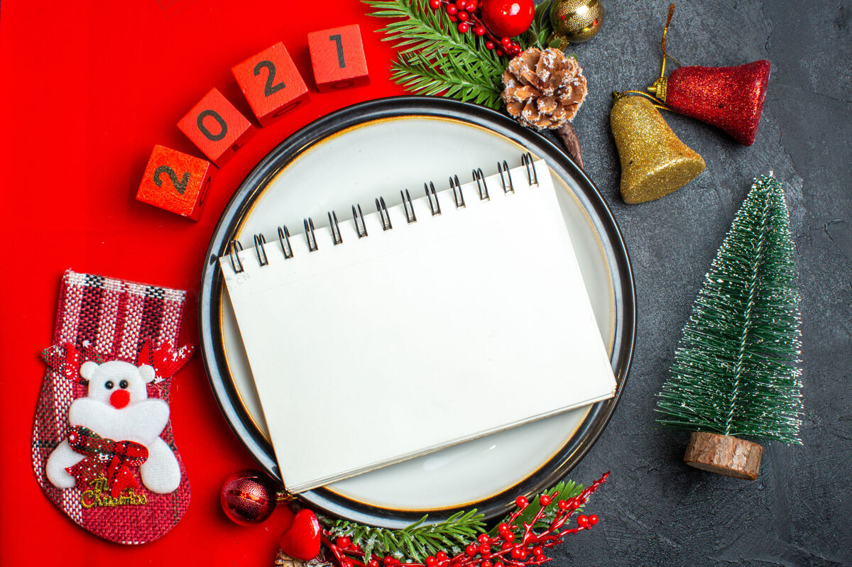 圣诞节新年背景俯视图 餐盘上有笔记本 装饰配件杉木树枝 黑色桌子上圣诞树旁的红色餐巾上有数字顶部餐巾树枝