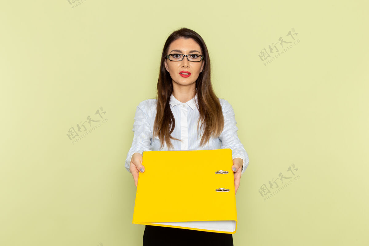业务身穿白衬衫和黑裙子的女上班族手持黄色文件站在绿色墙上的正视图前面文件工作