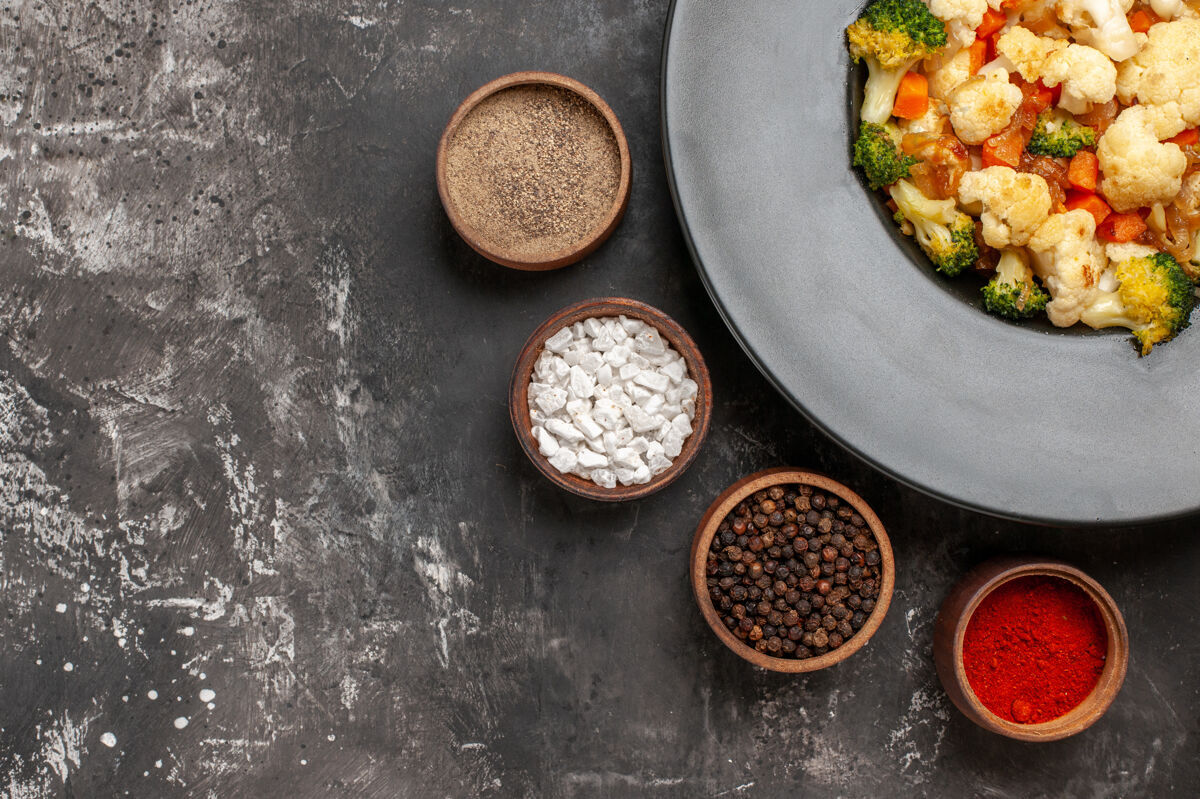 沙拉顶视图西兰花和花椰菜沙拉在黑色碗不同的香料碗在黑暗的表面碗胡椒顶部
