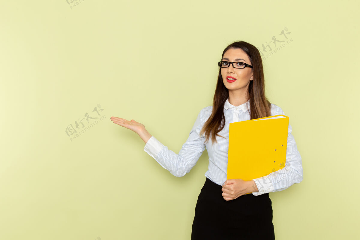 衬衫身穿白衬衫和黑裙子的女上班族手持黄色文件站在绿色墙上的正视图微笑文件女性