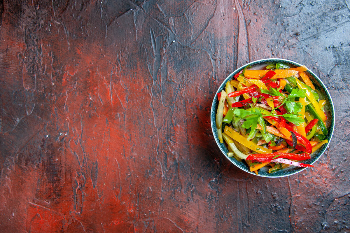 辣椒顶视图蔬菜沙拉碗在暗红色的桌子上与自由空间餐烹饪盘子