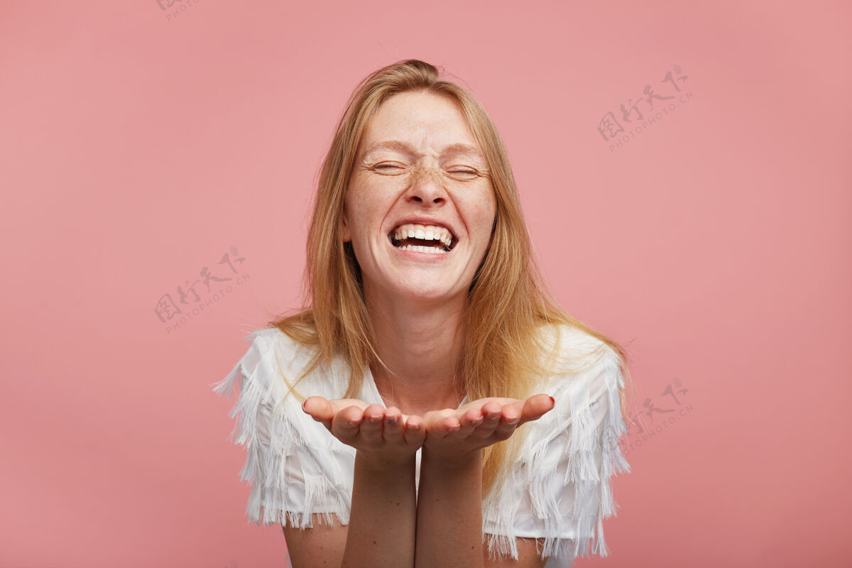 女士摄影棚拍摄的年轻快乐的女性 狐狸精的头发抬起她的手掌 站在粉红色的背景上 闭上眼睛 面带微笑 精神高昂长表情姿势