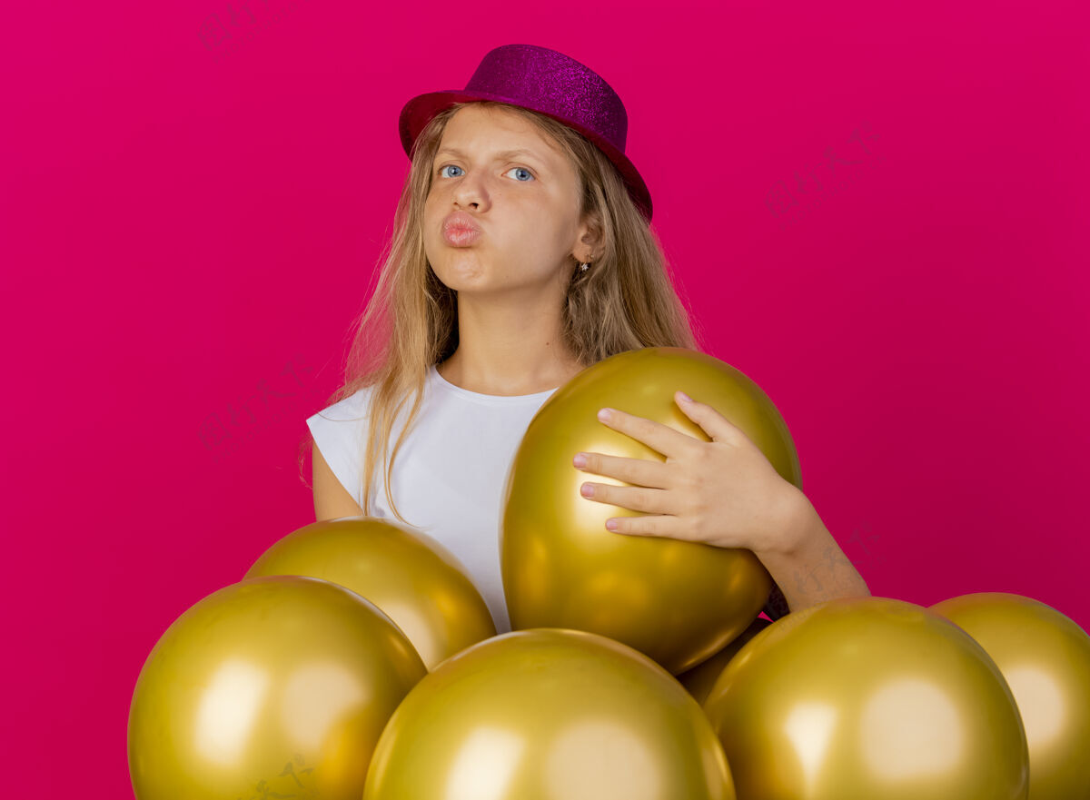 束戴着节日礼帽的漂亮小女孩 一群巴龙在一旁吹着飞吻 生日派对的概念站在粉色背景上巴隆站着小
