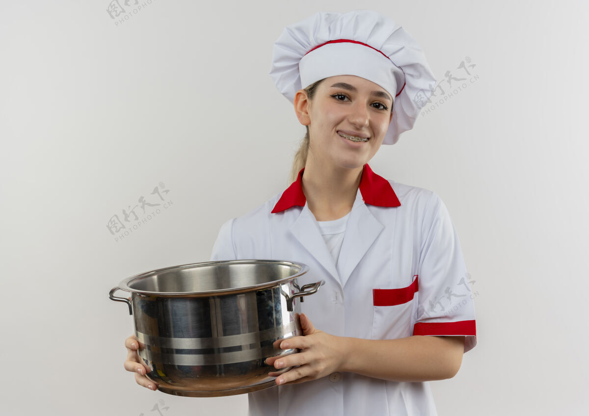 牙套面带微笑的年轻漂亮厨师穿着厨师制服 戴着牙套 拿着一个看起来孤立的罐子站在白色的空间里持有年轻大麻