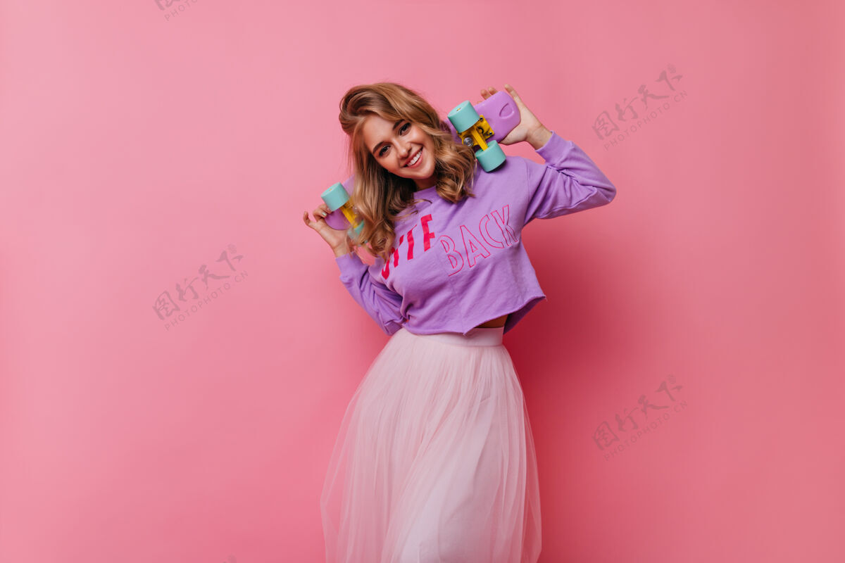 成人快乐的白人女士玩得开心热情的金发女孩站在粉红色的滑板上现代肖像室内