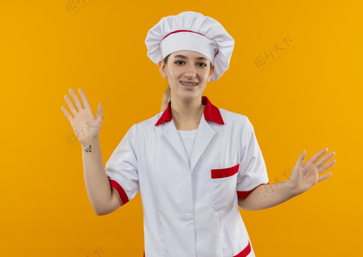年轻微笑着的年轻漂亮厨师身着厨师制服 戴着牙套 两手空空的 孤立在橙色的空间里空微笑显示