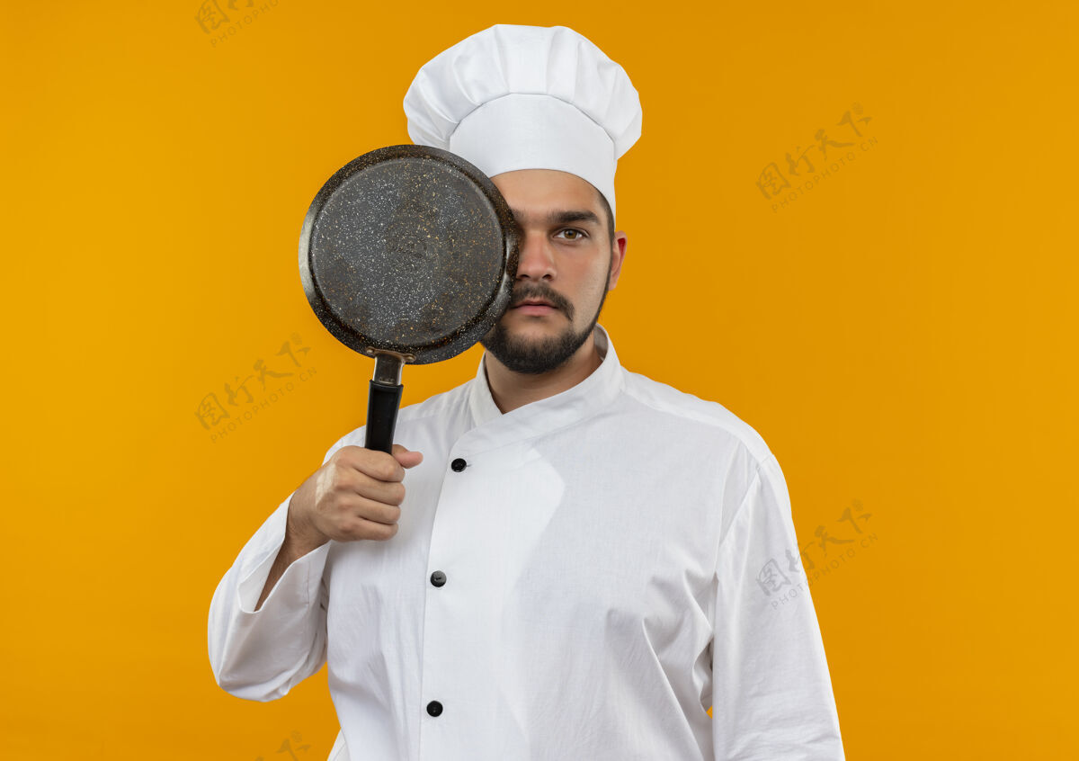 看身穿厨师制服的年轻男厨师手拿煎锅 从后面看 被隔离在橙色的空间里拿着橙子平底锅