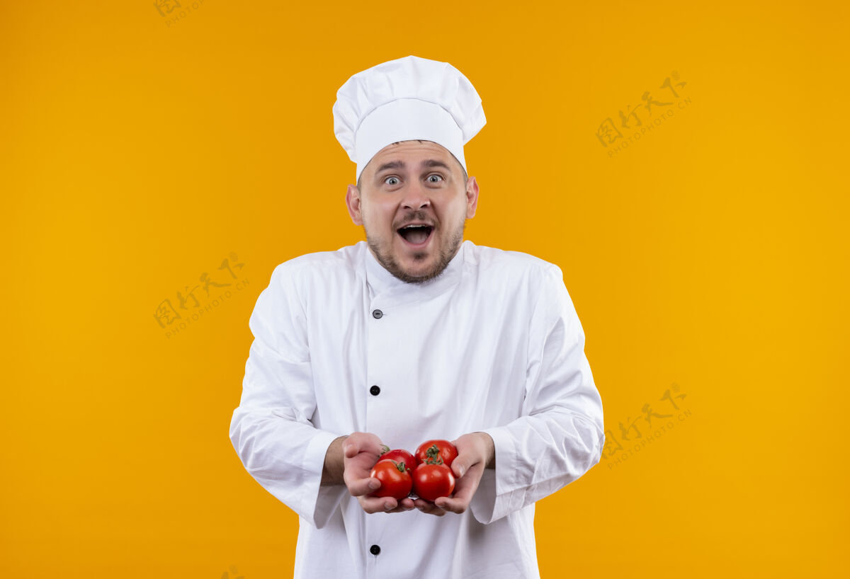 惊讶年轻帅气的厨师穿着厨师制服 手里拿着西红柿隔离在橙色的空间里帅哥厨师拿着