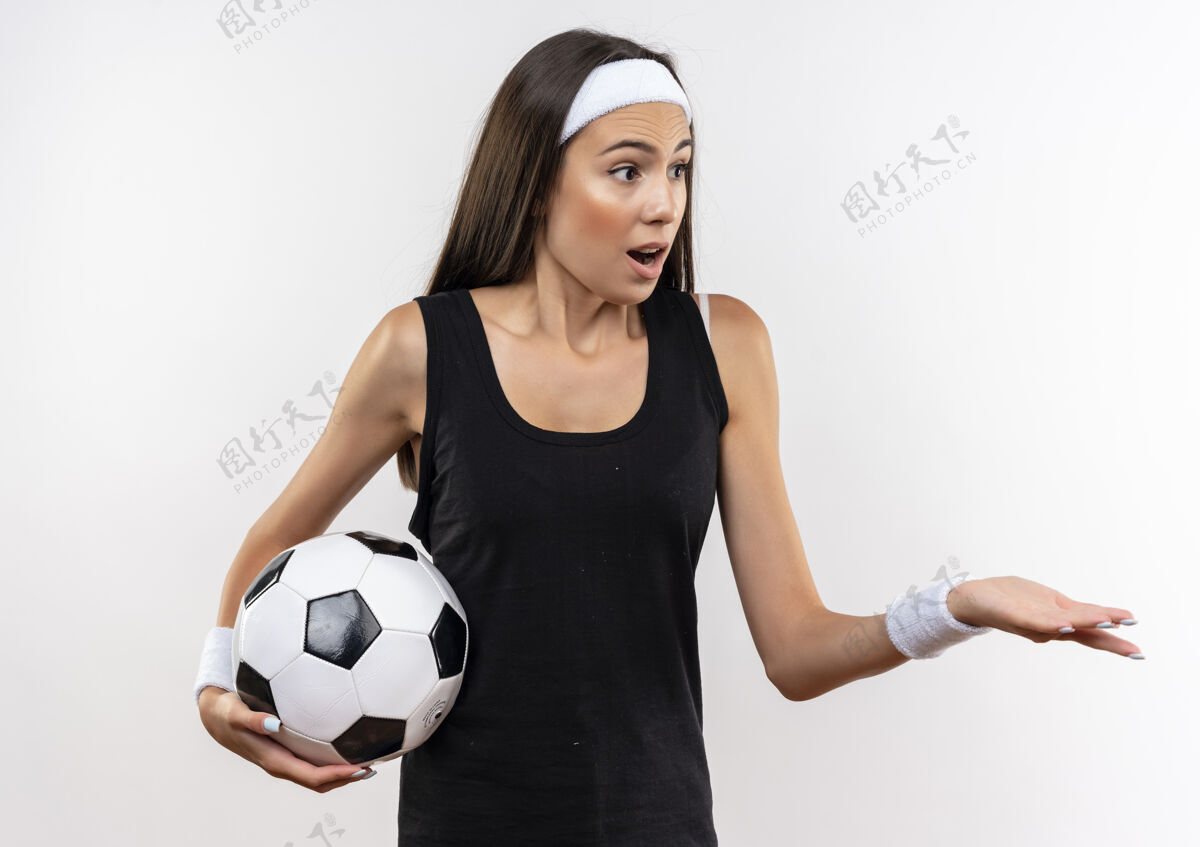 头带惊讶漂亮的运动女孩戴着头带和腕带拿着足球看一边 显示空手孤立在白色空间腕带足球漂亮