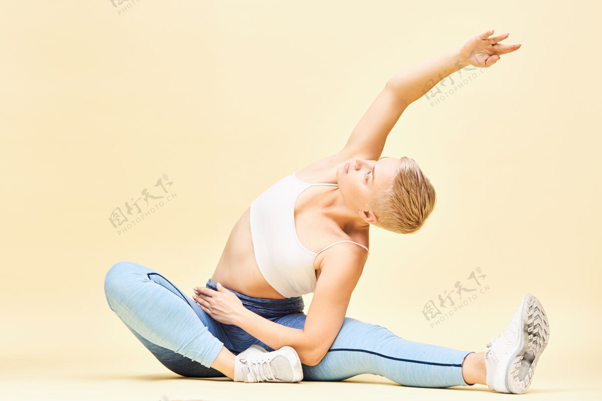 柔韧运动灵活的年轻女性 穿着时尚的运动服 坐着做瑜伽 侧弯 伸展肋骨 一只手向上男孩女孩练习普拉提 坐在地板上 伸展弯曲运动健身房