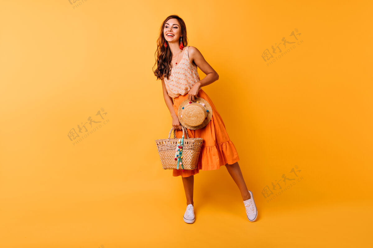 连衣裙充满灵感的夏日配饰女人的全长镜头穿着橙色裙子的快乐姜黄色女模特拿着帽子和包模特帽子时尚