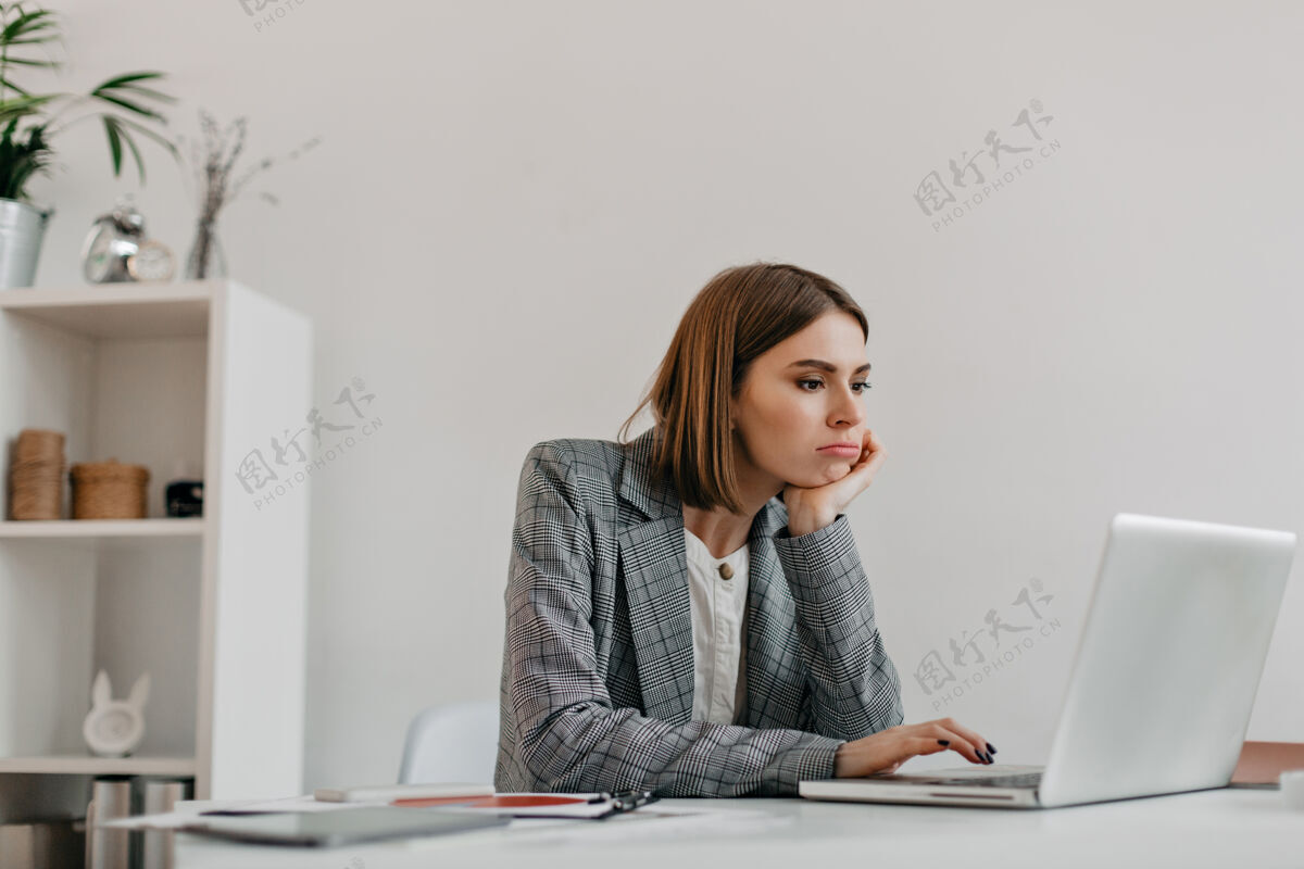 成功穿着灰色套装的无聊的年轻商务女士在工作场所看着笔记本电脑屏幕长相灰色年轻
